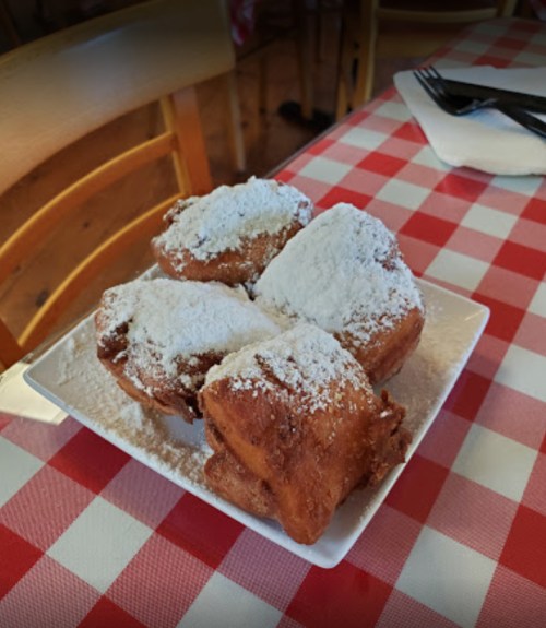 A plate of four powdered sugar-dusted pastries on a red and white checkered tablecloth.
