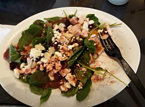 A plate of spinach salad with feta cheese, diced chicken, nuts, and a vinaigrette dressing, partially eaten.