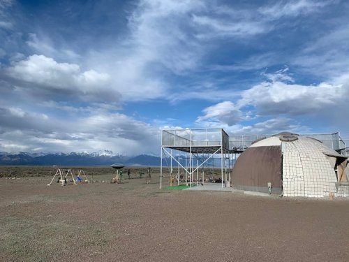 A dome-shaped structure with a playground nearby, set against a backdrop of mountains and a cloudy sky.