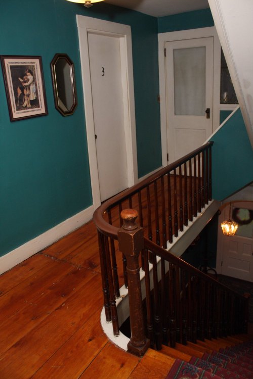 A staircase with a wooden railing, leading to a door labeled "3," against a teal wall and wooden floor.