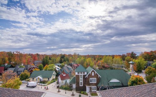 Aerial view of a colorful autumn landscape with houses and trees under a cloudy sky.