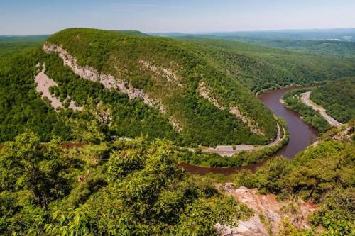 A scenic view of a winding river surrounded by lush green hills and trees under a clear blue sky.