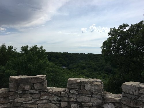 A stone wall overlooks a lush green landscape under a partly cloudy sky.