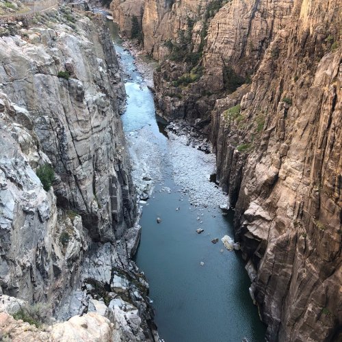 Aerial view of a narrow river winding through steep, rocky canyon walls under a clear sky.