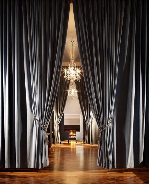 Elegant room entrance framed by dark curtains, featuring a chandelier and a cozy fireplace in the background.