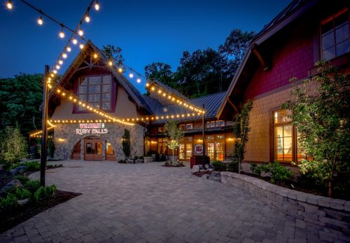 A charming building with string lights at dusk, featuring a welcoming entrance to Ruby Falls surrounded by greenery.