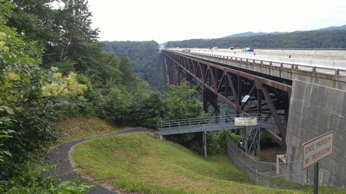A tall bridge spans a valley, surrounded by lush greenery and a winding path leading to a viewing area below.