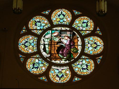 Stained glass window depicting two figures in a circular design with floral patterns and vibrant colors.