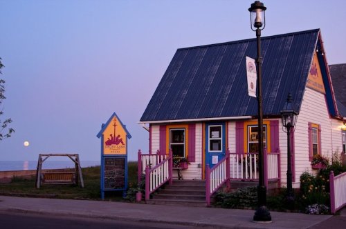 A charming, colorful house with a blue roof, porch, and a swing, set against a twilight sky with a rising moon.