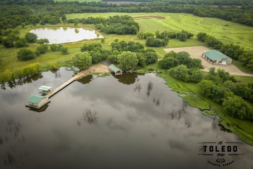 Aerial view of a serene landscape with a pond, lush greenery, and a small dock in Toledo, Kansas.