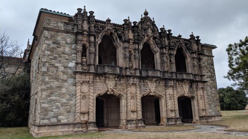 Ornate stone building with intricate carvings and arched windows, set against a cloudy sky.