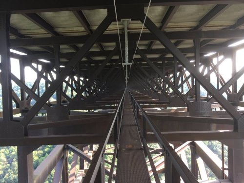 View looking down the metal framework of a bridge, showcasing beams and supports against a green landscape below.