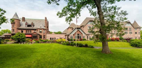 A large, elegant mansion with a tower, surrounded by lush green lawns and colorful gardens.