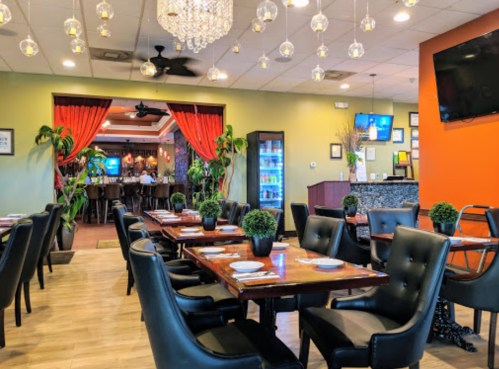 Interior of a restaurant featuring elegant decor, wooden tables, black chairs, and a bar area in the background.