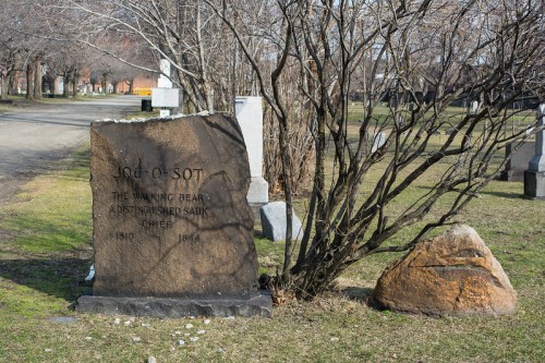 A weathered gravestone for Jo-o-sot, a distinguished Sauk chief, surrounded by bare trees in a cemetery.