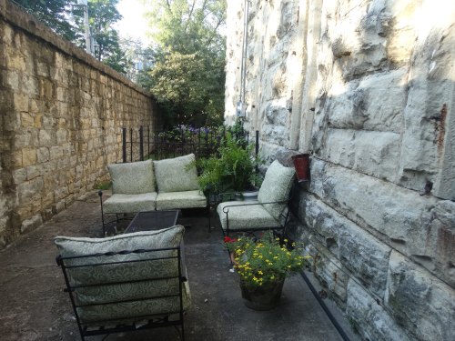 A cozy outdoor seating area with green cushions, surrounded by plants and a stone wall.