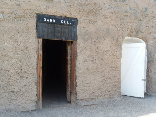 Entrance to a historic building labeled "Dark Cell," featuring a wooden door and a white side door.