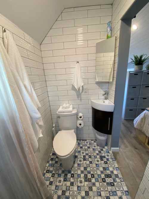 A small bathroom featuring a toilet, sink, and shower with white tiled walls and a patterned floor.