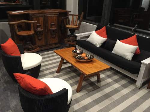 Cozy living area with a black sofa, orange and white cushions, a wooden coffee table, and a rustic bar in the background.