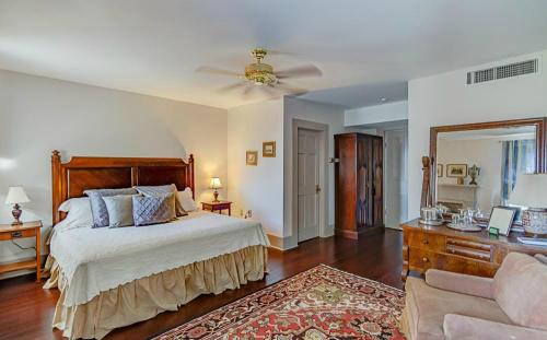 Cozy bedroom with a wooden bed, soft lighting, a mirror, and a plush armchair, featuring warm tones and a decorative rug.