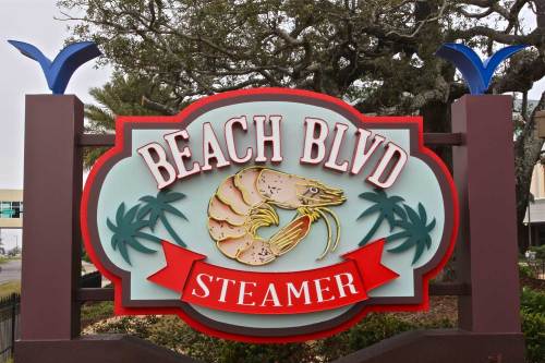 Colorful sign for "Beach Blvd Steamer" featuring a shrimp and palm trees, set against a natural backdrop.