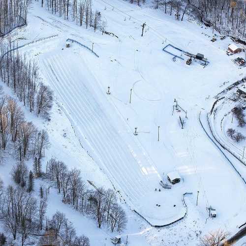 Aerial view of a snowy landscape with ski slopes, trees, and a ski lift in a winter setting.