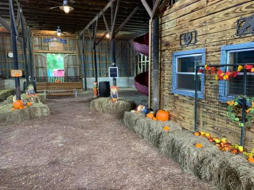 A rustic barn interior decorated with hay bales, pumpkins, and scarecrows, creating a festive autumn atmosphere.