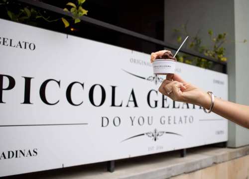 A hand holding a cup of gelato in front of a sign for Piccola Gelato.