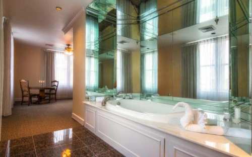 A spacious bathroom with a large mirror, a bathtub, and a towel shaped like a swan, featuring natural light from windows.