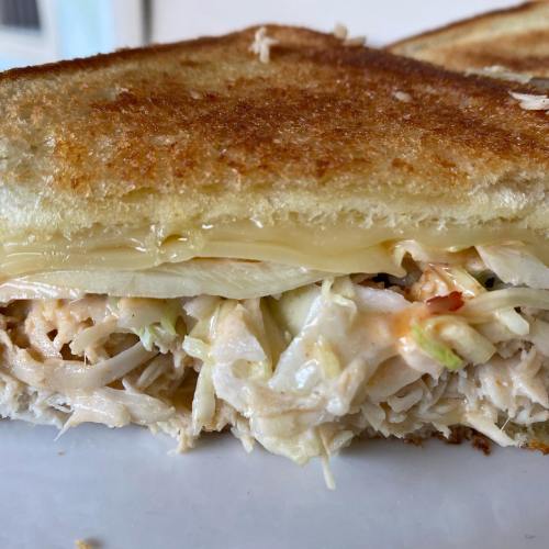 Close-up of a toasted sandwich filled with shredded chicken and melted cheese, showcasing a golden-brown crust.