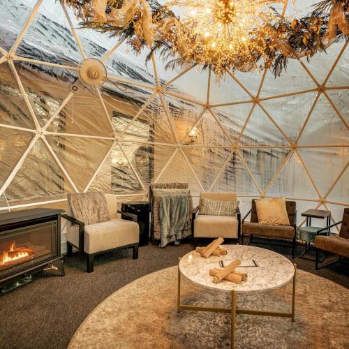 Cozy indoor dome with plush seating, a marble table, and a warm fireplace, adorned with decorative lighting.