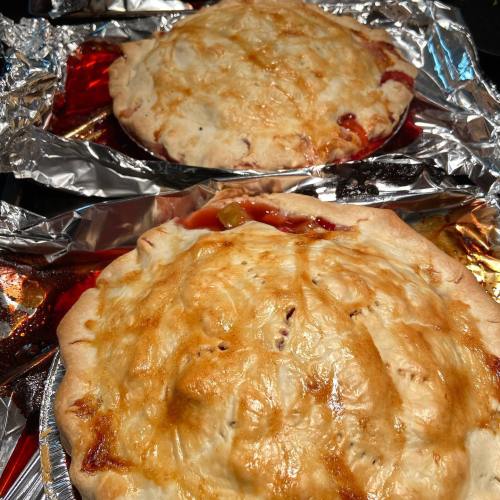 Two freshly baked fruit pies with golden crusts, resting on shiny foil-lined baking sheets.