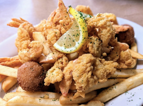 A plate of crispy fried shrimp and fries, garnished with a lemon wedge and parsley, alongside two hushpuppies.