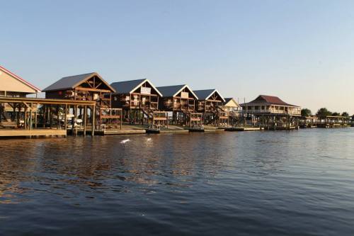 Row of wooden houses on stilts along a calm waterway, with clear blue skies in the background.