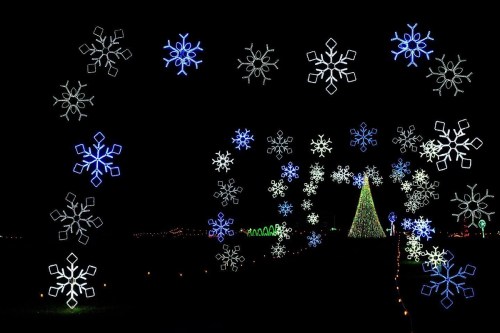 A festive scene featuring a decorated Christmas tree surrounded by glowing snowflake lights against a dark background.