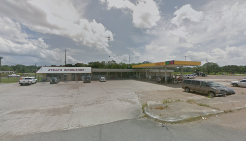 A supermarket with a gas station, featuring a large parking lot and a cloudy sky in the background.