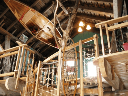 A rustic interior with wooden structures, a canoe hanging from the ceiling, and various handcrafted items.