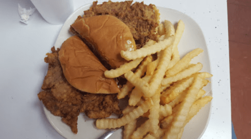 A plate with two sandwich buns, fried chicken, and crinkle-cut fries.