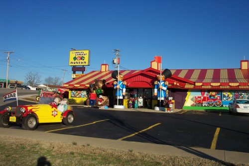 Colorful exterior of a large toy museum with playful sculptures and a vintage car in the foreground. Clear blue sky above.