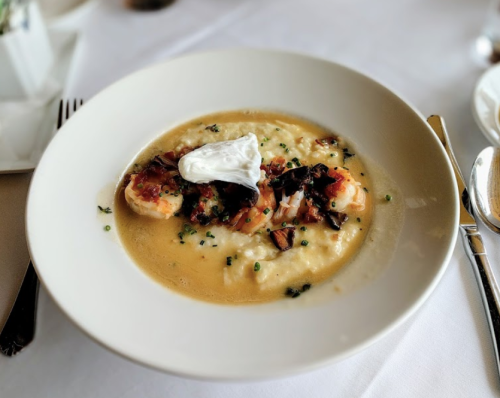 A bowl of creamy grits topped with shrimp, bacon, and a poached egg, garnished with chives.