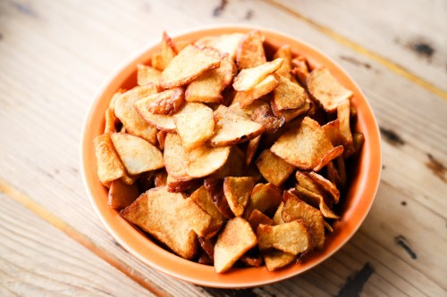 A bowl of crispy, golden-brown potato chips on a wooden surface.