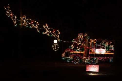 A brightly lit truck decorated with holiday lights, featuring reindeer and festive figures, set against a dark background.