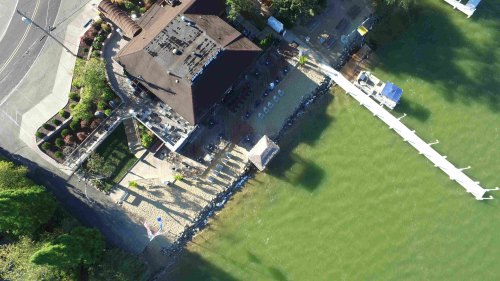 Aerial view of a lakeside restaurant with a dock, surrounded by greenery and a sandy area.