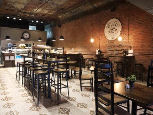 A cozy café with wooden tables, high chairs, and a brick wall featuring a smiling face artwork.