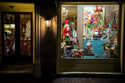 A festive shop window displays colorful holiday decorations, including nutcrackers, ornaments, and a vibrant painting.