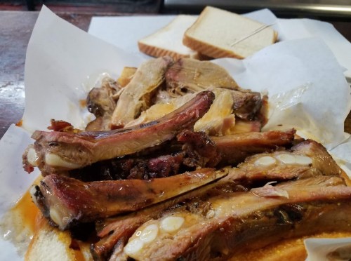 A plate of tender, sauced ribs with slices of white bread on the side, served on parchment paper.