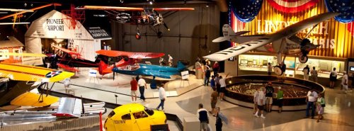 A vibrant aviation museum display featuring vintage airplanes, exhibits, and visitors exploring the aircraft.