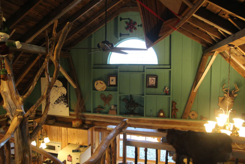 Interior of a rustic cabin with wooden beams, green walls, and various decorative items displayed on shelves.