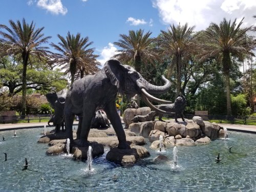 A fountain featuring elephant sculptures surrounded by palm trees and a clear blue sky.