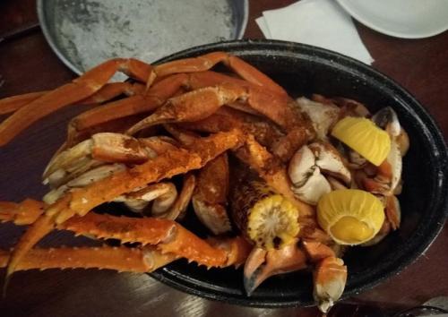 A black dish filled with seasoned crabs, corn, and lemon wedges on a wooden table.
